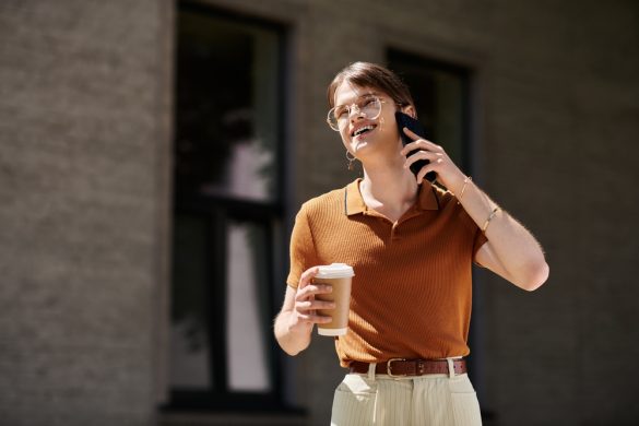 A smiling person walking outdoors, holding a coffee and talking on the phone