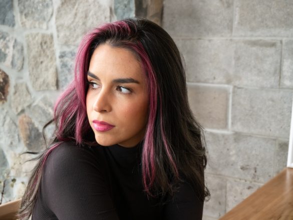 A woman with pink highlights in her hair looks away thoughtfully