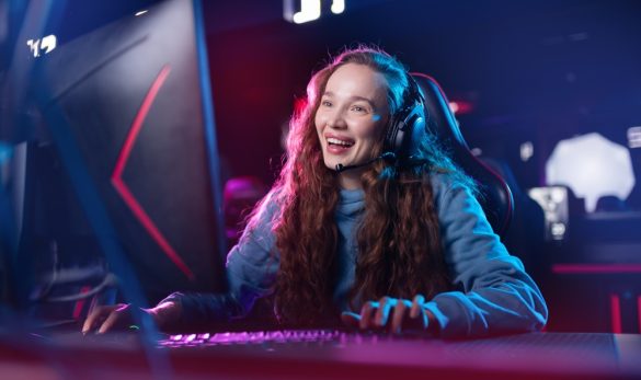 A smiling person with long hair sitting at a gaming computer.