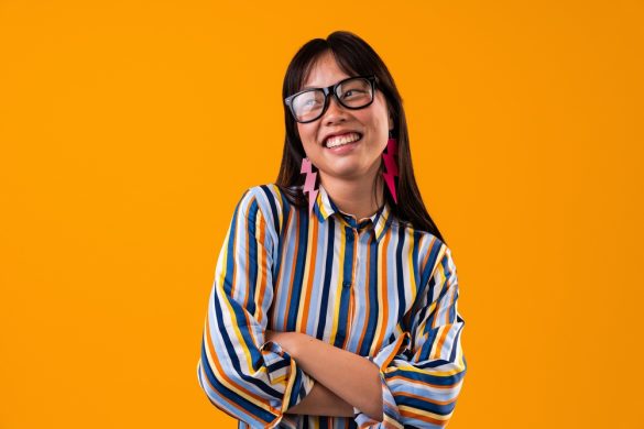 A smiling woman with a striped shirt, glasses and lightning bolt earrings, with her arms folded