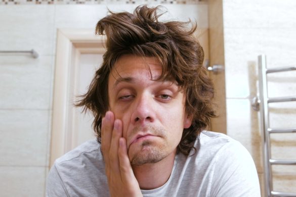 A person with messy hair rubbing their face and looking tired