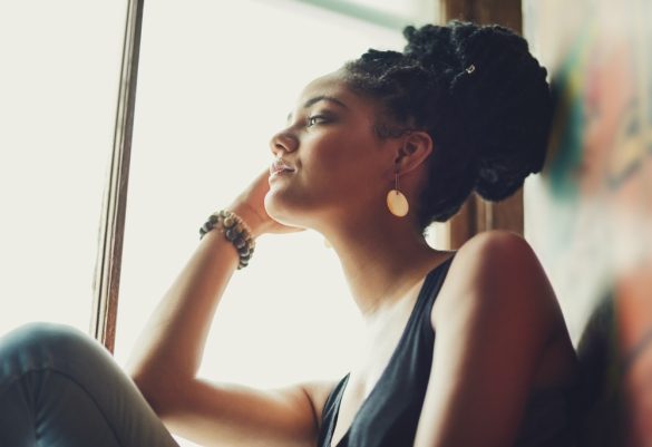 A person sits by a window looking into the distance with their face resting on one hand