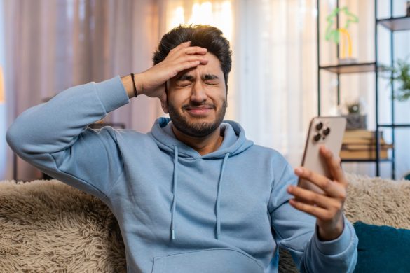 A man holding a phone, grimacing as if he has just made a mistake