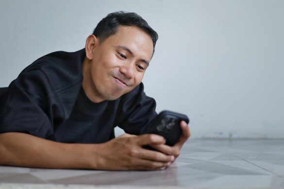 A person lies on the floor, smiling at their phone
