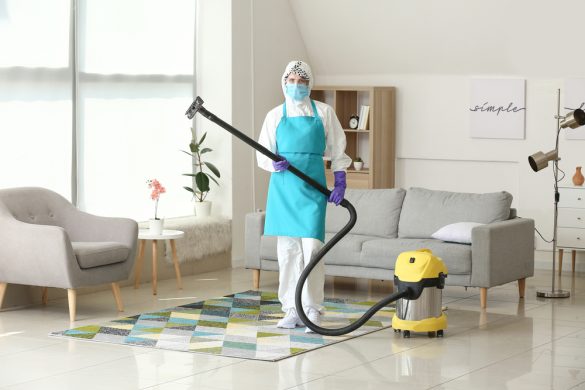 A person standing in a living room wearing full protective gear while holding the handle of a vacuum cleaner