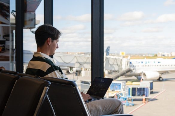 A man sitting in an airport lounge typing on a laptop